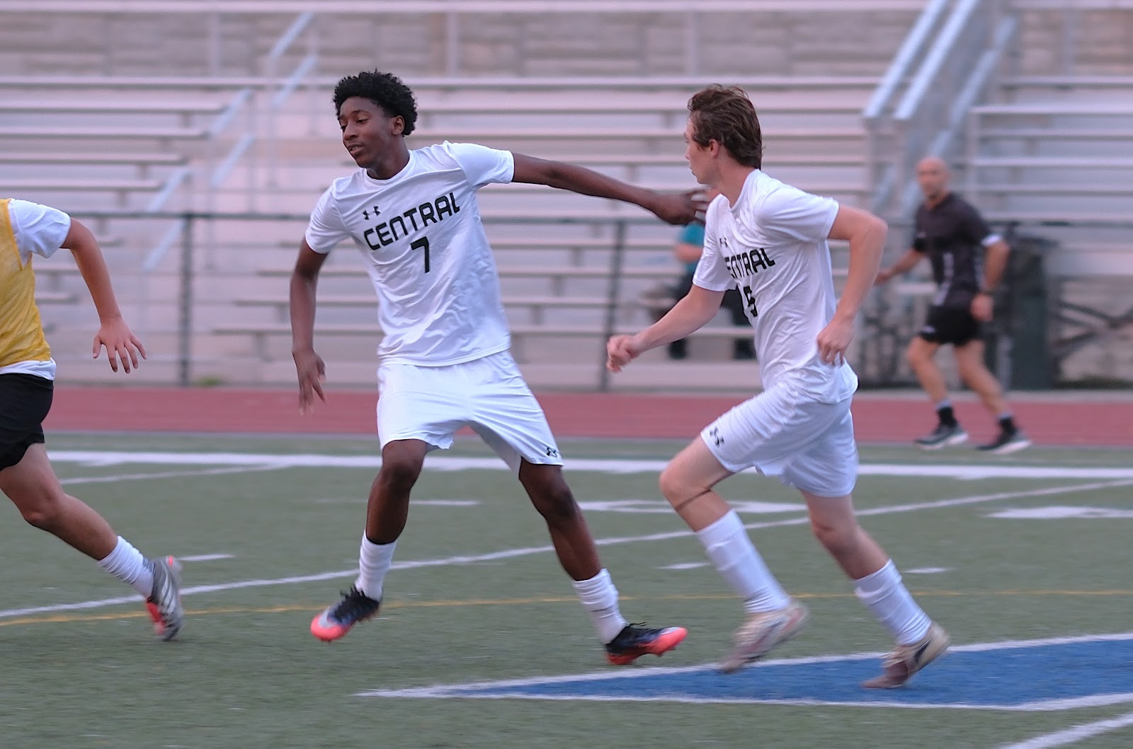 Two Central boys' soccer players running together on the field in white away kits