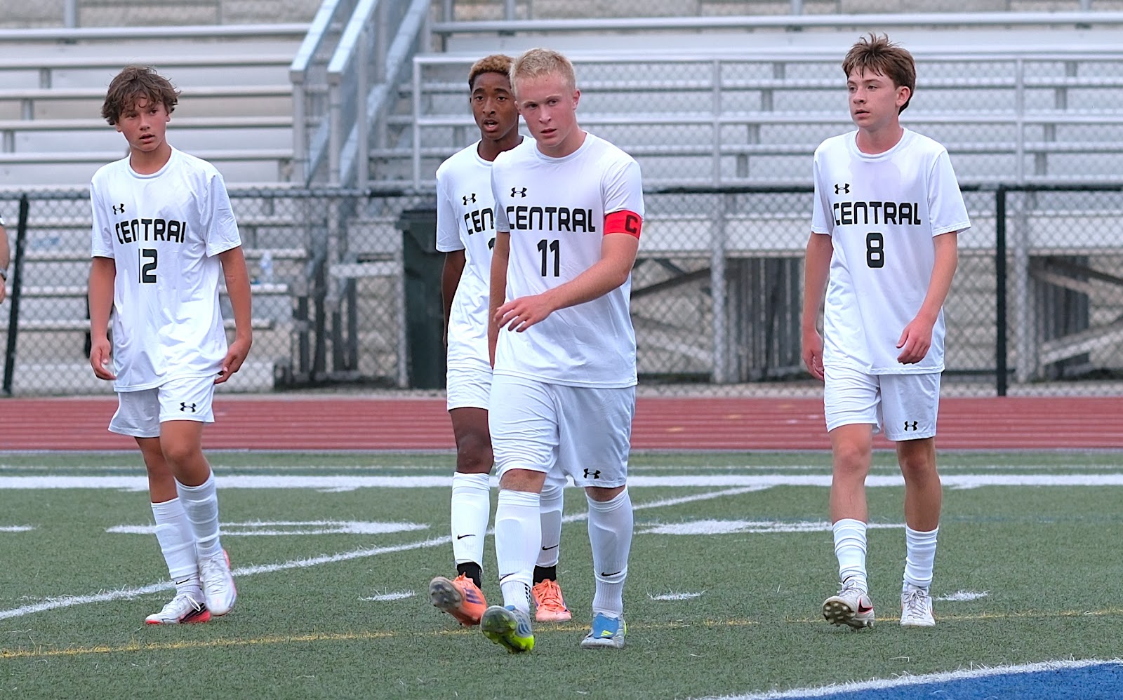 Four Central boys' soccer players walking together on the field in white away kits